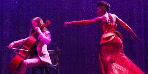 Scène du Paradis Latin : violoncelliste et chanteuse en robe rouge dans le show L'Oiseau Paradis