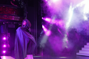 La sorcière de Mon Premier Cabaret au Paradis Latin, entourée de fumée et de lumières violettes, spectacle familial pour enfants dès 3 ans